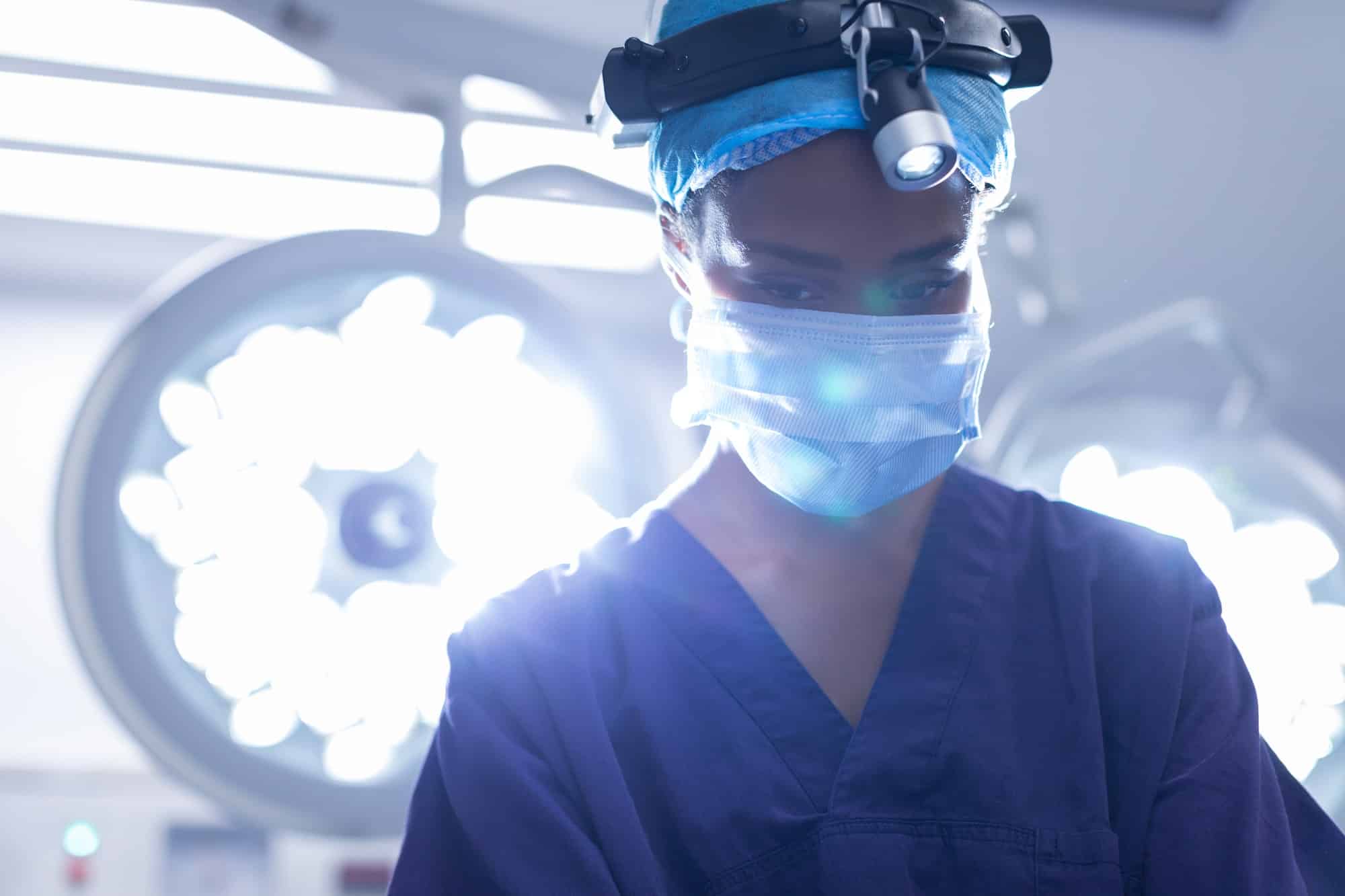 Young Mixed-race female with surgical headlight performing operation in operation theater